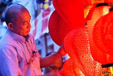 Asian man around retirement age standing next to glowing lanterns.